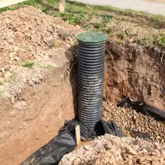 Czarna rura drenarska na metry z zieloną pokrywą, umieszczona w wykopie z żwirem i geowłókniną.